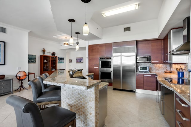 kitchen with pendant lighting, sink, appliances with stainless steel finishes, a kitchen breakfast bar, and wall chimney exhaust hood