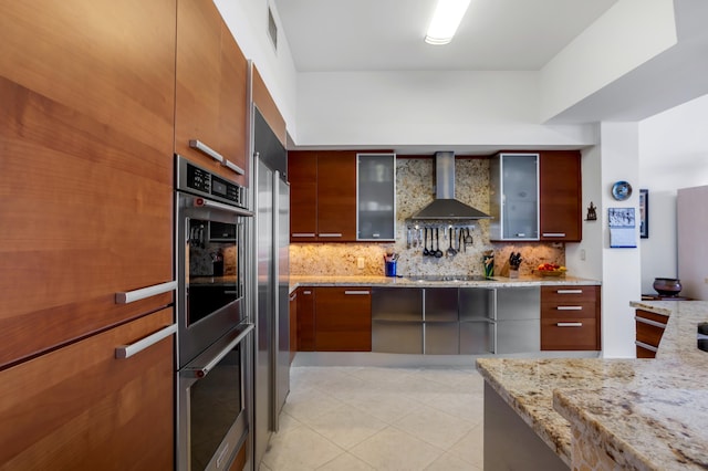 kitchen featuring light stone counters, light tile patterned floors, tasteful backsplash, and wall chimney exhaust hood