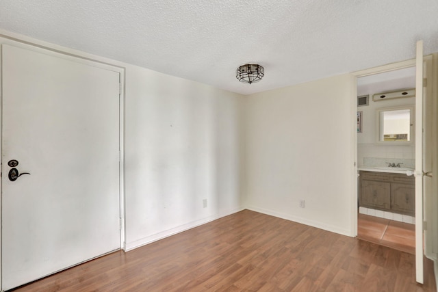 unfurnished bedroom with ensuite bathroom, wood-type flooring, sink, and a textured ceiling