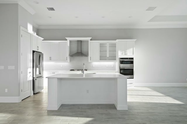 kitchen featuring sink, white cabinetry, a center island with sink, appliances with stainless steel finishes, and wall chimney range hood