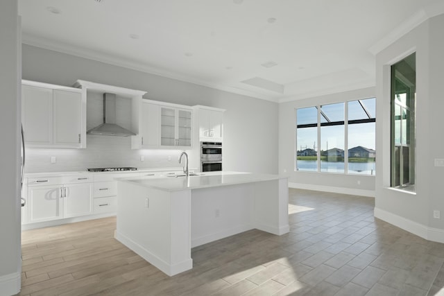 kitchen featuring white cabinetry, an island with sink, gas stovetop, a water view, and wall chimney exhaust hood