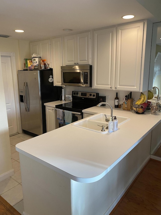 kitchen with stainless steel appliances, kitchen peninsula, sink, and white cabinets