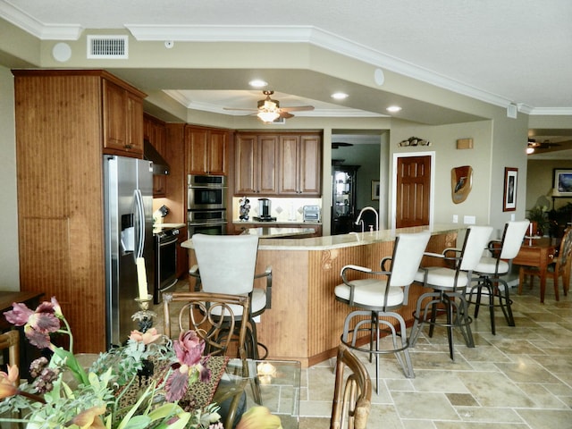 kitchen with stainless steel appliances, ornamental molding, a breakfast bar area, and ceiling fan