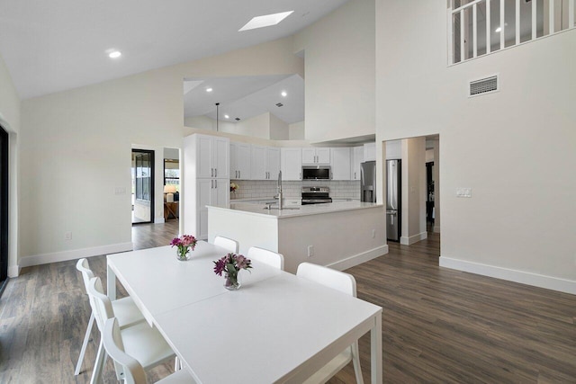 dining room with dark wood-type flooring, high vaulted ceiling, a skylight, and sink