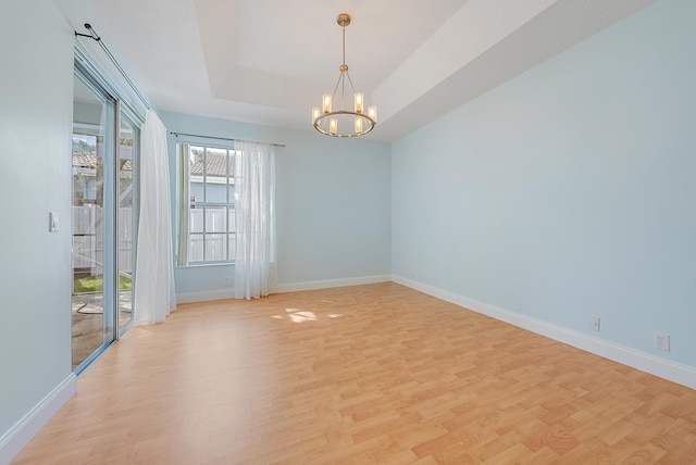 spare room featuring a chandelier, a raised ceiling, and light wood-type flooring