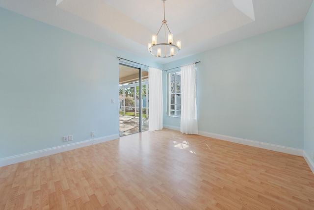 unfurnished room with a notable chandelier, a tray ceiling, and light wood-type flooring