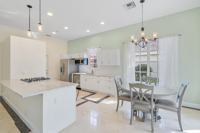 kitchen featuring white cabinetry, appliances with stainless steel finishes, light stone countertops, and hanging light fixtures