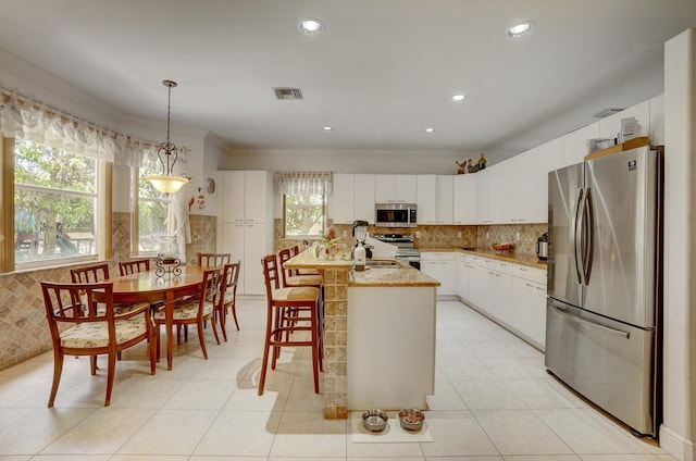 kitchen featuring white cabinetry, an island with sink, stainless steel appliances, hanging light fixtures, and crown molding