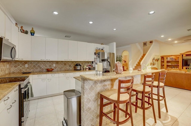 kitchen with appliances with stainless steel finishes, a center island, white cabinetry, tasteful backsplash, and a breakfast bar area