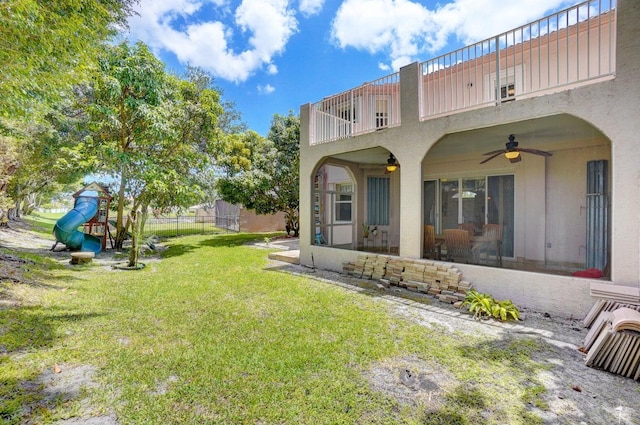 rear view of property with ceiling fan, a lawn, a balcony, and a playground