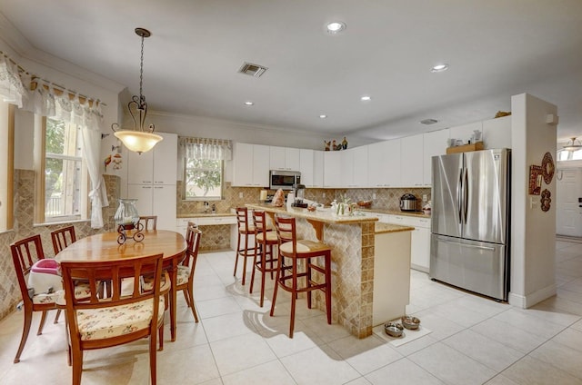 kitchen with pendant lighting, white cabinets, appliances with stainless steel finishes, an island with sink, and ornamental molding