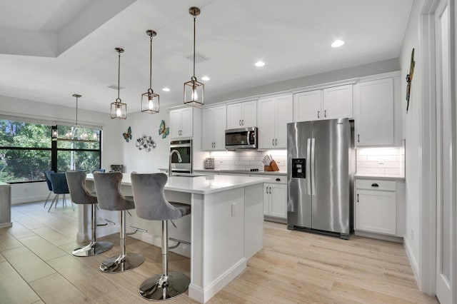 kitchen with decorative light fixtures, tasteful backsplash, white cabinetry, a kitchen island with sink, and stainless steel appliances