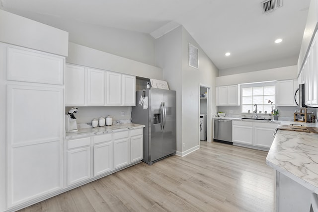 kitchen featuring washer / dryer, sink, white cabinetry, appliances with stainless steel finishes, and light stone counters