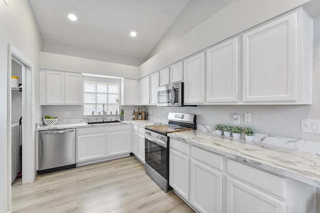 kitchen with light hardwood / wood-style floors, stainless steel appliances, vaulted ceiling, white cabinets, and sink