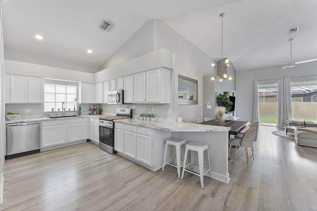 kitchen featuring decorative light fixtures, kitchen peninsula, white cabinetry, stainless steel appliances, and high vaulted ceiling