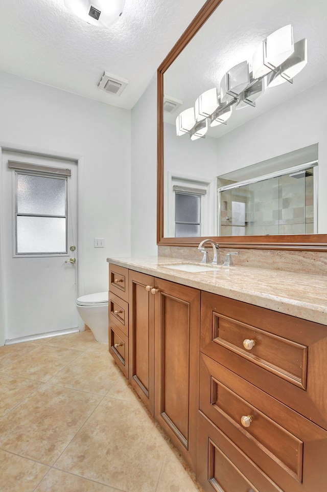 bathroom with a textured ceiling, tile patterned flooring, vanity, toilet, and walk in shower