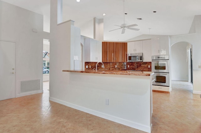 kitchen featuring kitchen peninsula, ceiling fan, appliances with stainless steel finishes, backsplash, and white cabinetry