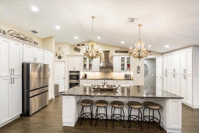 kitchen featuring a breakfast bar area, stainless steel appliances, wall chimney range hood, white cabinetry, and a large island with sink