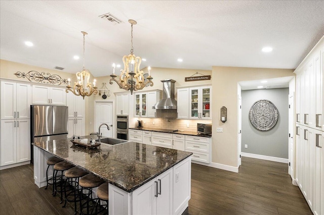 kitchen featuring a center island with sink, wall chimney exhaust hood, stainless steel appliances, vaulted ceiling, and sink