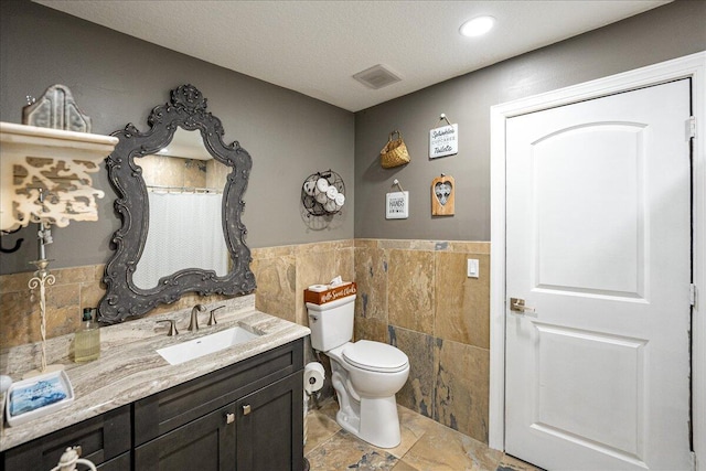 bathroom featuring tile walls, vanity, toilet, and a textured ceiling