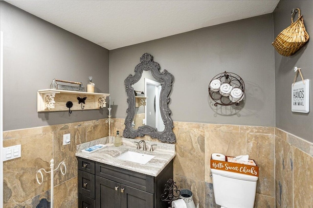 bathroom featuring tile walls, vanity, toilet, and a textured ceiling