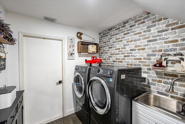 clothes washing area featuring dark hardwood / wood-style flooring, brick wall, sink, and washer and clothes dryer