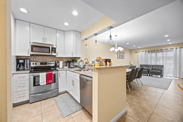 kitchen with pendant lighting, kitchen peninsula, sink, appliances with stainless steel finishes, and white cabinets