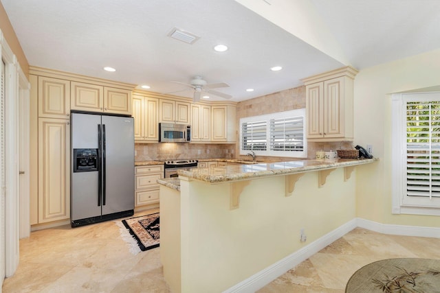 kitchen featuring a breakfast bar area, stainless steel appliances, cream cabinets, light stone countertops, and kitchen peninsula