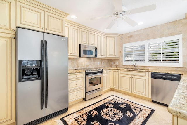 kitchen featuring sink, stainless steel appliances, cream cabinetry, and light stone countertops