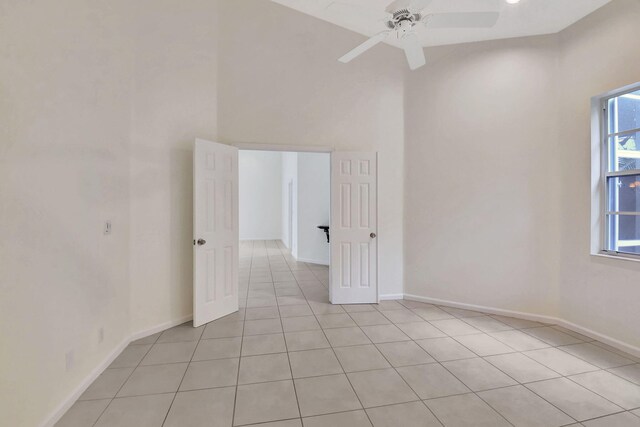 tiled empty room with ceiling fan and a towering ceiling