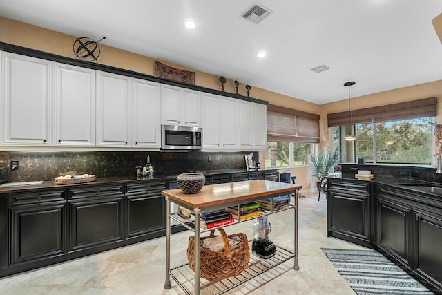 kitchen with dark countertops, white cabinetry, stainless steel microwave, and tasteful backsplash