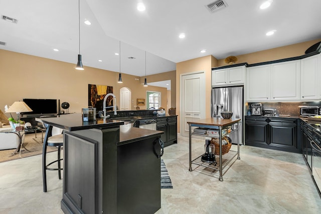 kitchen featuring pendant lighting, appliances with stainless steel finishes, white cabinetry, an island with sink, and a breakfast bar