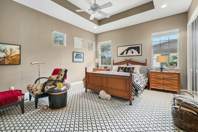 bedroom featuring ceiling fan, multiple windows, and a tray ceiling