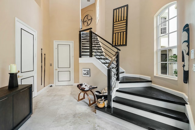 stairway featuring a healthy amount of sunlight, a towering ceiling, and baseboards