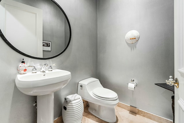 half bath with a sink, tile patterned flooring, toilet, and baseboards