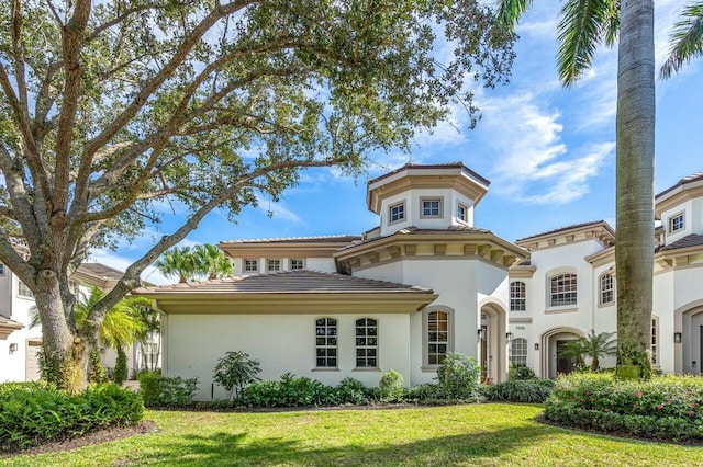 mediterranean / spanish-style home featuring a front lawn, a tile roof, and stucco siding