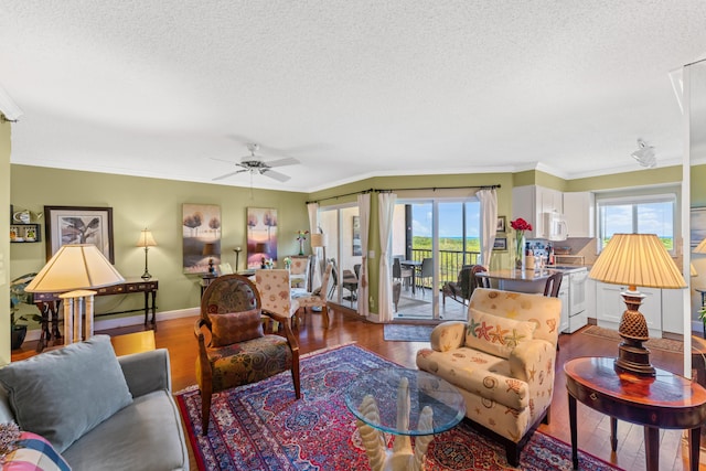 living room featuring ceiling fan, ornamental molding, wood-type flooring, and a textured ceiling