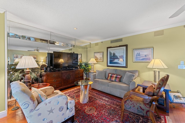 living room featuring ceiling fan, hardwood / wood-style flooring, a textured ceiling, and ornamental molding