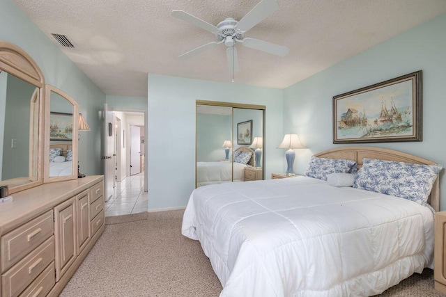 bedroom featuring a textured ceiling, light colored carpet, a closet, and ceiling fan