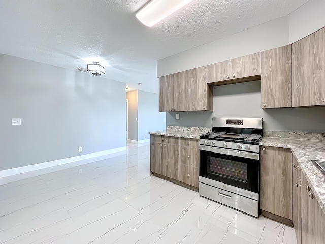 kitchen with a textured ceiling, stainless steel range with gas stovetop, and light stone countertops