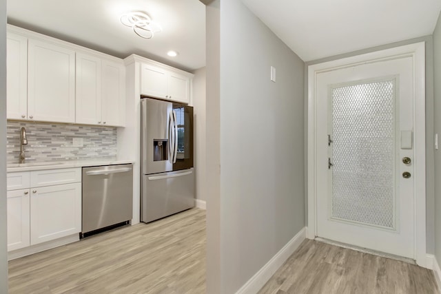 kitchen with sink, light hardwood / wood-style flooring, appliances with stainless steel finishes, white cabinets, and backsplash