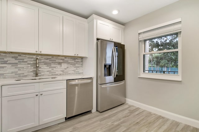 kitchen featuring sink, light hardwood / wood-style flooring, appliances with stainless steel finishes, white cabinetry, and tasteful backsplash