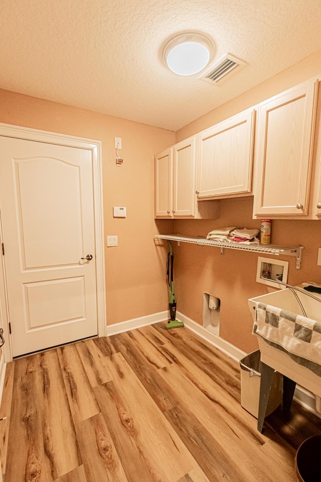 clothes washing area with cabinets, washer hookup, electric dryer hookup, a textured ceiling, and light hardwood / wood-style flooring