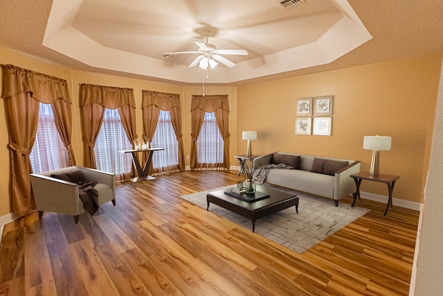 living room featuring a tray ceiling, ceiling fan, and light wood-type flooring