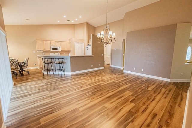 unfurnished living room with high vaulted ceiling, an inviting chandelier, and light wood-type flooring