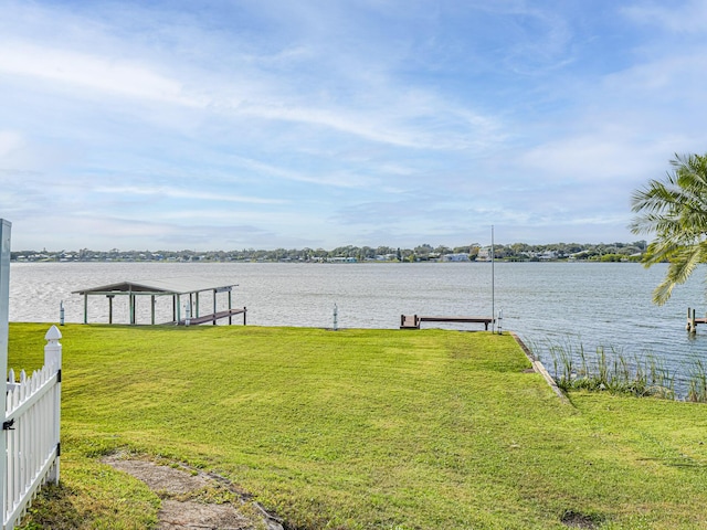 view of dock with a lawn, a water view, and fence