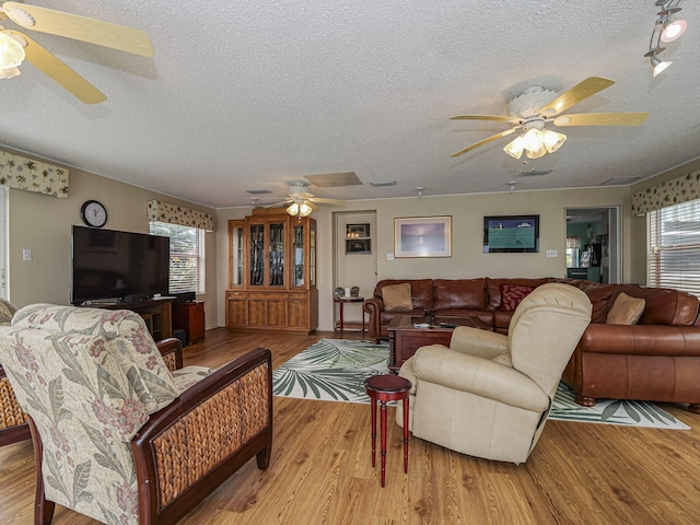 living area featuring a ceiling fan, plenty of natural light, a textured ceiling, and wood finished floors