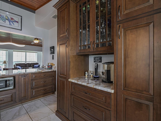 kitchen with visible vents, glass insert cabinets, stainless steel microwave, marble finish floor, and light stone countertops