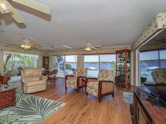 living room with a textured ceiling, light wood-type flooring, a ceiling fan, and wallpapered walls