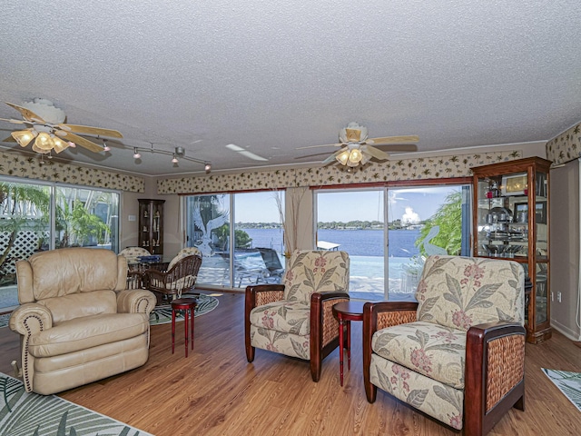 living room featuring a textured ceiling, a water view, wood finished floors, and a ceiling fan